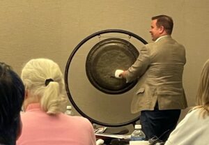 a man hits a gong while smiling